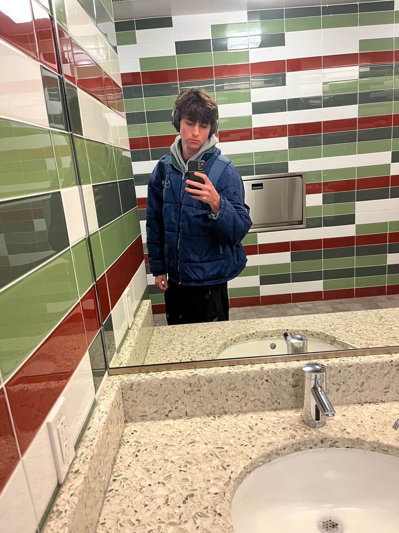 Kyle taking a mirror selfie in a blue jacket in a tiled bathroom